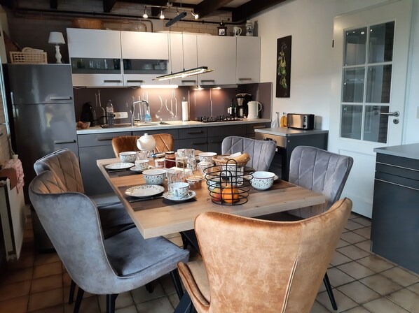 A modern kitchen with a dining table set for four, surrounded by grey and brown upholstered chairs.