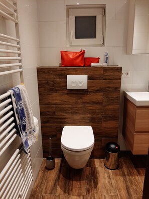 Ein modernes Badezimmer mit einer Wand in Holzoptik, einer weißen Toilette, einem Handtuchhalter mit einem gemusterten Handtuch und einer kleinen Mülltonne.