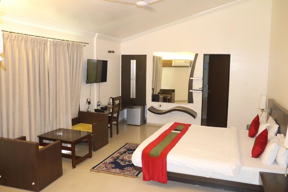 Habitación de hotel con cama, escritorio, silla, televisor y espejo.