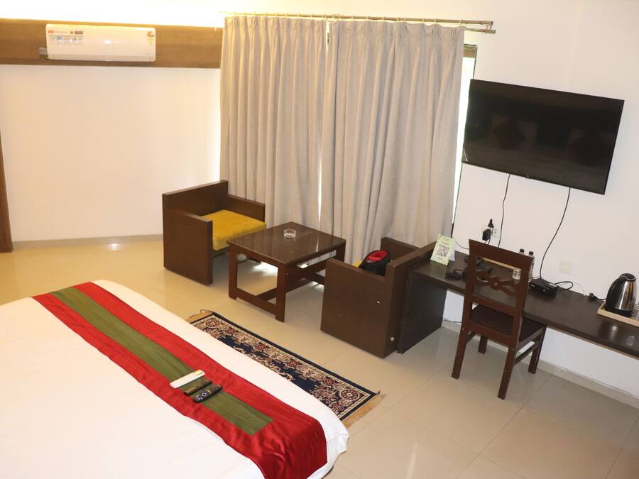 Habitación de hotel con cama, escritorio, silla, televisor y cafetera.