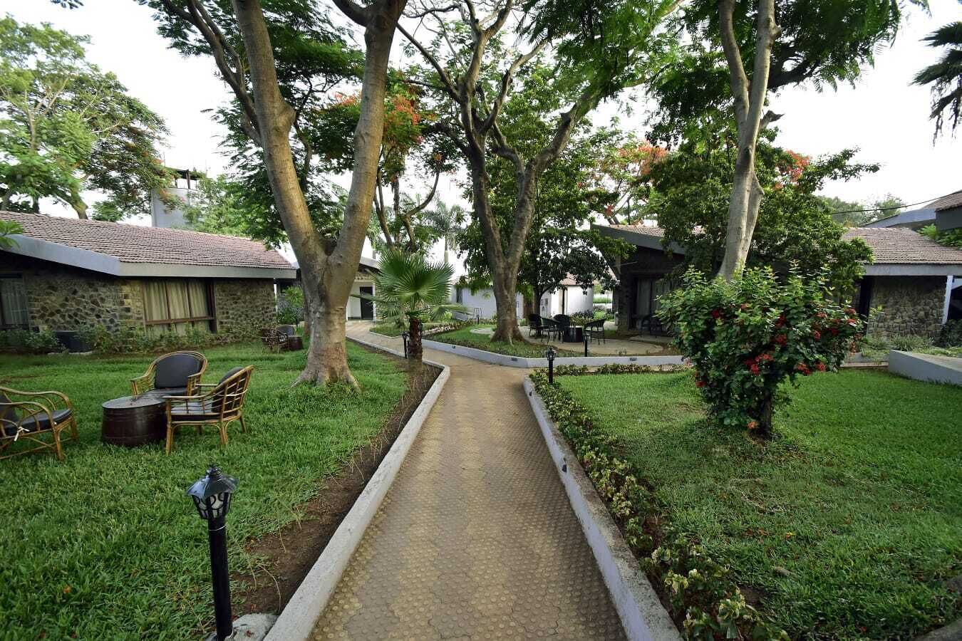 Un chemin menant à un bâtiment doté d’un toit en tuiles, entouré d’une végétation luxuriante et d’arbres.