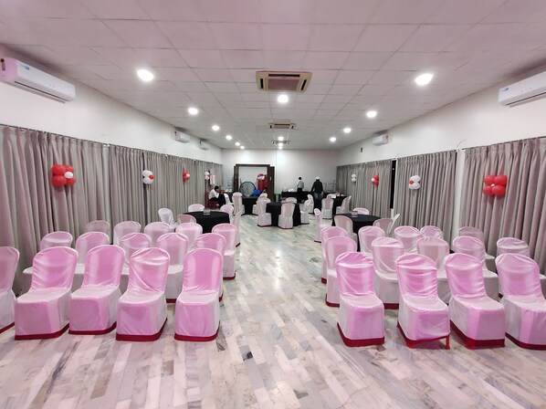 Un salón de conferencias con filas de sillas, mesas y unidades de aire acondicionado.