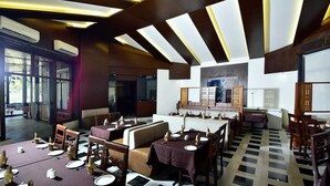 Un restaurante con suelo de espinilla, varias mesas de comedor con manteles blancos y un diseño de techo moderno.