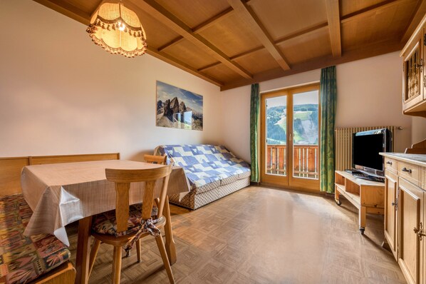 Une pièce avec un plafond en bois, une table recouverte d’une nappe, un lit avec une couverture à carreaux, un téléviseur et une fenêtre donnant sur l’extérieur.