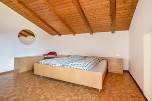 Une chambre avec un plafond en bois, un miroir rond, un lit avec une couette à carreaux, une chaise et deux tables de chevet.
