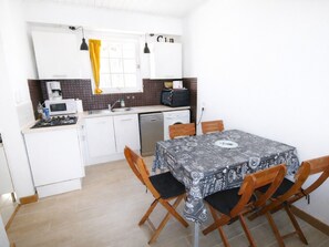 A compact kitchen with white cabinets, a microwave, a sink, and a table with a patterned tablecloth.