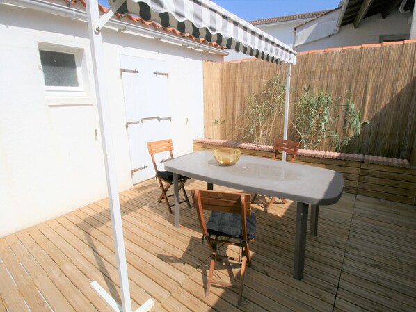 An outdoor patio with a table and chairs, a wooden fence, and a white door.