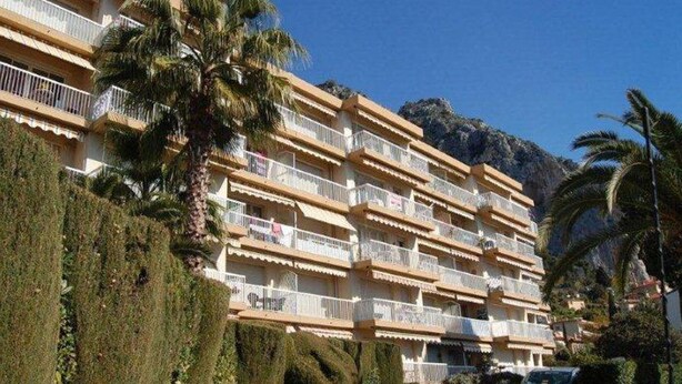 Et hotel med flere etager og balkoner, omgivet af velplejede hække og palmer.