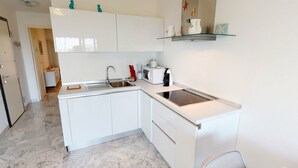 Et lille køkken med hvide skabe, en indbygget komfur, en vask og en lille bordplade.