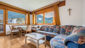 Un accogliente soggiorno con divano, tavolo da pranzo con sedie e ampie finestre vista montagna.