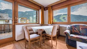 Una stanza con pavimento in legno, un tavolo con sedie, un divano e ampie finestre con vista sulle montagne.