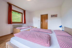 A bedroom with two beds, a window with curtains, a door, and a small table.