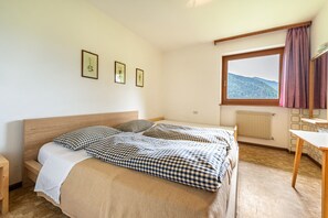 Un dormitorio con cama, ventana con vistas, un radiador y una mesita.