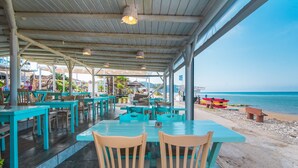 An outdoor restaurant with tables and chairs, overlooking a beach with boats. - Studio 'Mirage Arillas Studio Type A8' with Sea View, Pool & Wi-Fi (corfu)