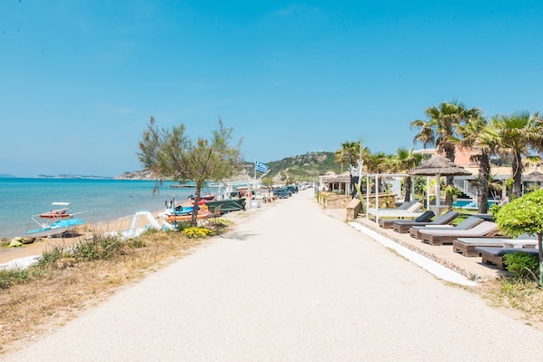 A beach path with lounge chairs and umbrellas, boats, and a clear view of the sea.