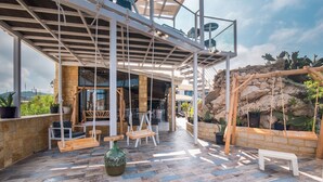 An outdoor patio with a wooden floor, seating areas, a swing, and a view of the surrounding landscape. - 'Mirage Arillas Studio Type A9' next to Beach with Balcony, Shared Pool & Wi-Fi (corfu)