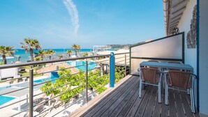 Ein Balkon mit Blick auf Pool und Strand, mit Metallstühlen und einem Tisch.