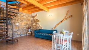 Eine Wendeltreppe, eine Steinwand, ein blaues Sofa, ein Esstisch mit Stühlen und eine Holzbalkendecke.
