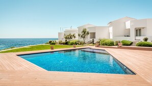 A modern house with a swimming pool, a view of the sea, and a well-maintained garden.