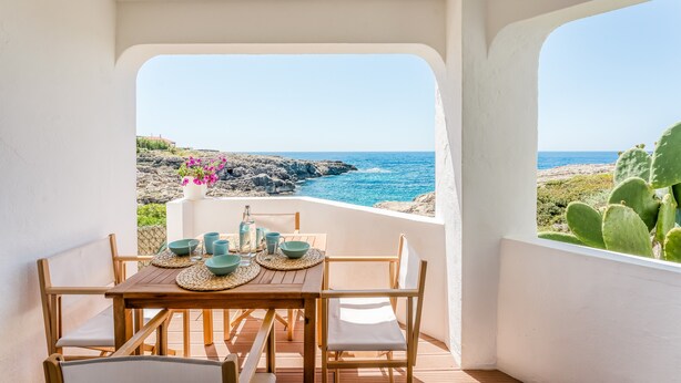 A wooden table with chairs and a view of the sea.