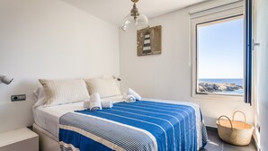 A bedroom with a bed, a window with a view, a wall-mounted light fixture, and a wall decoration.