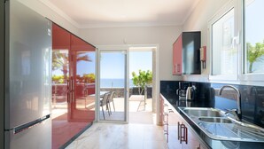 A modern kitchen with a view of the sea, a sliding glass door, and a dining area with outdoor seating. - Vacation Rental 'Villa Loretta' with Sea View, Heated Pool & Wi-Fi (Puerto del Carmen)