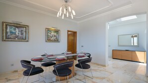 A dining area with a glass table, four chairs, and a chandelier. There are two framed artworks on the wall, a wooden door, and a large mirror. - Vacation Rental 'Villa Loretta' with Sea View, Heated Pool & Wi-Fi (Puerto del Carmen)