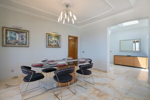 A dining area with a glass table, four chairs, and a chandelier. There are two framed artworks on the wall, a wooden door, and a large mirror. - Vacation Rental 'Villa Loretta' with Sea View, Heated Pool & Wi-Fi (Puerto del Carmen)