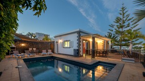 A swimming pool with lounge chairs, a covered patio, and a building with a glass door. - Vacation Rental 'Villa Loretta' with Sea View, Heated Pool & Wi-Fi (Puerto del Carmen)