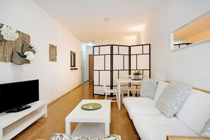 A modern living room with a flat-screen TV, a white sofa, a dining table with chairs, and a partition wall.