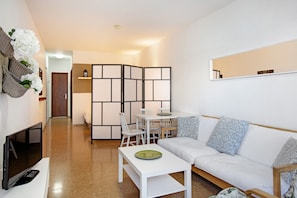 A modern living room with a sofa, a coffee table, a TV, and a dining area with chairs and a table.