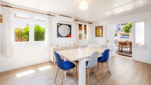 A dining area with a wooden table and chairs, large windows with curtains, and artwork on the walls.