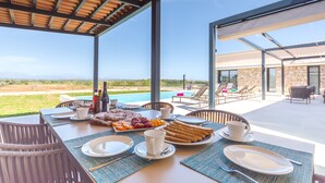 Un espace extérieur aménagé pour les repas, avec vue sur la piscine, des chaises en osier et une table dressée pour le petit-déjeuner.