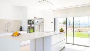 Une cuisine moderne dotée d’un grand îlot central, d’un four encastré et offrant une vue sur le jardin extérieur.