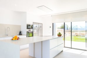 A modern kitchen with a large island, a built-in oven, and a view of the outdoor garden.