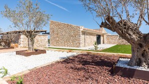 Un bâtiment moderne aux murs en pierre, doté d’une terrasse en pierre et abritant un grand arbre.
