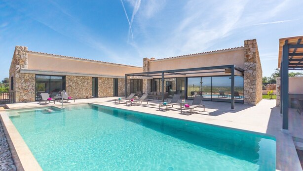 Un espace piscine moderne, doté de chaises longues et d’une façade en pierre.