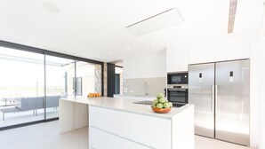 Une cuisine moderne dotée d’un grand îlot central, d’appareils électroménagers en acier inoxydable et d’une porte en verre donnant sur un balcon.