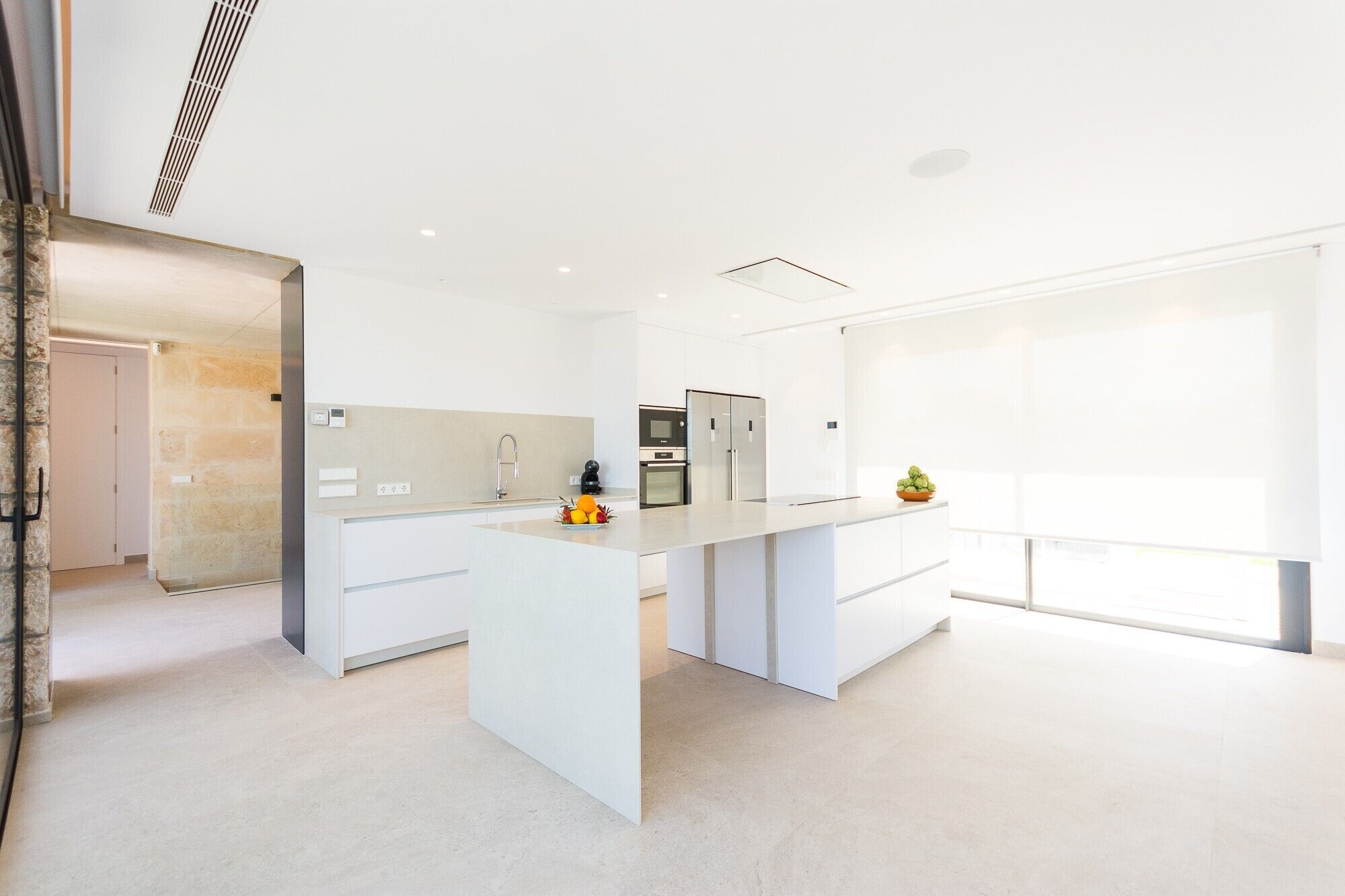 A modern kitchen with white cabinetry, a central island, a built-in oven, and a refrigerator.
