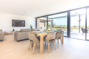 Un salon moderne comprenant un coin repas, de grandes portes vitrées donnant sur un espace extérieur et un téléviseur à écran plat fixé au mur.