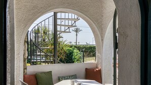 A balcony with a white table, a sofa with cushions, and a view of a spiral staircase and greenery. - Apartment 'ART-Apartamentos Revilla Tacke E' with Shared Pool & Wi-Fi (Empuriabrava)