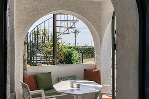 Un balcon avec une table blanche, un canapé avec des coussins et une vue sur un escalier en colimaçon et de la verdure.