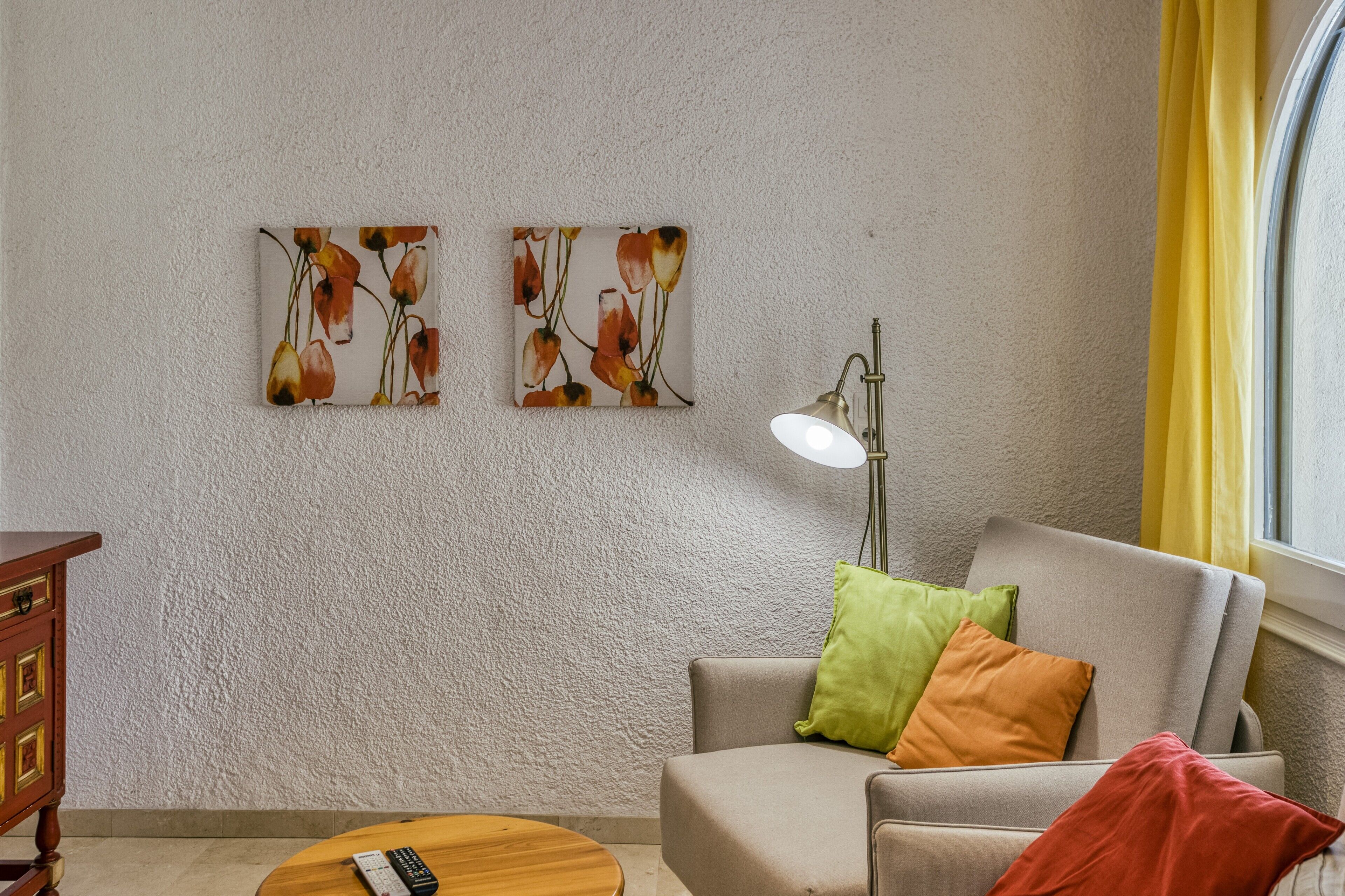 Ein Wohnzimmer mit Sofa, einer Lampe, einer Fernbedienung und Kunstwerken an der Wand.
