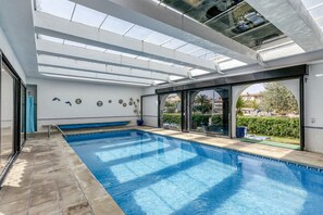 Una piscina con techo de vidrio, una banca y vistas al exterior.