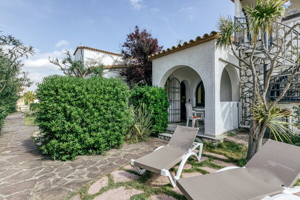 Un patio con suelo de piedra, un edificio blanco con arcos y dos sillones de descanso.