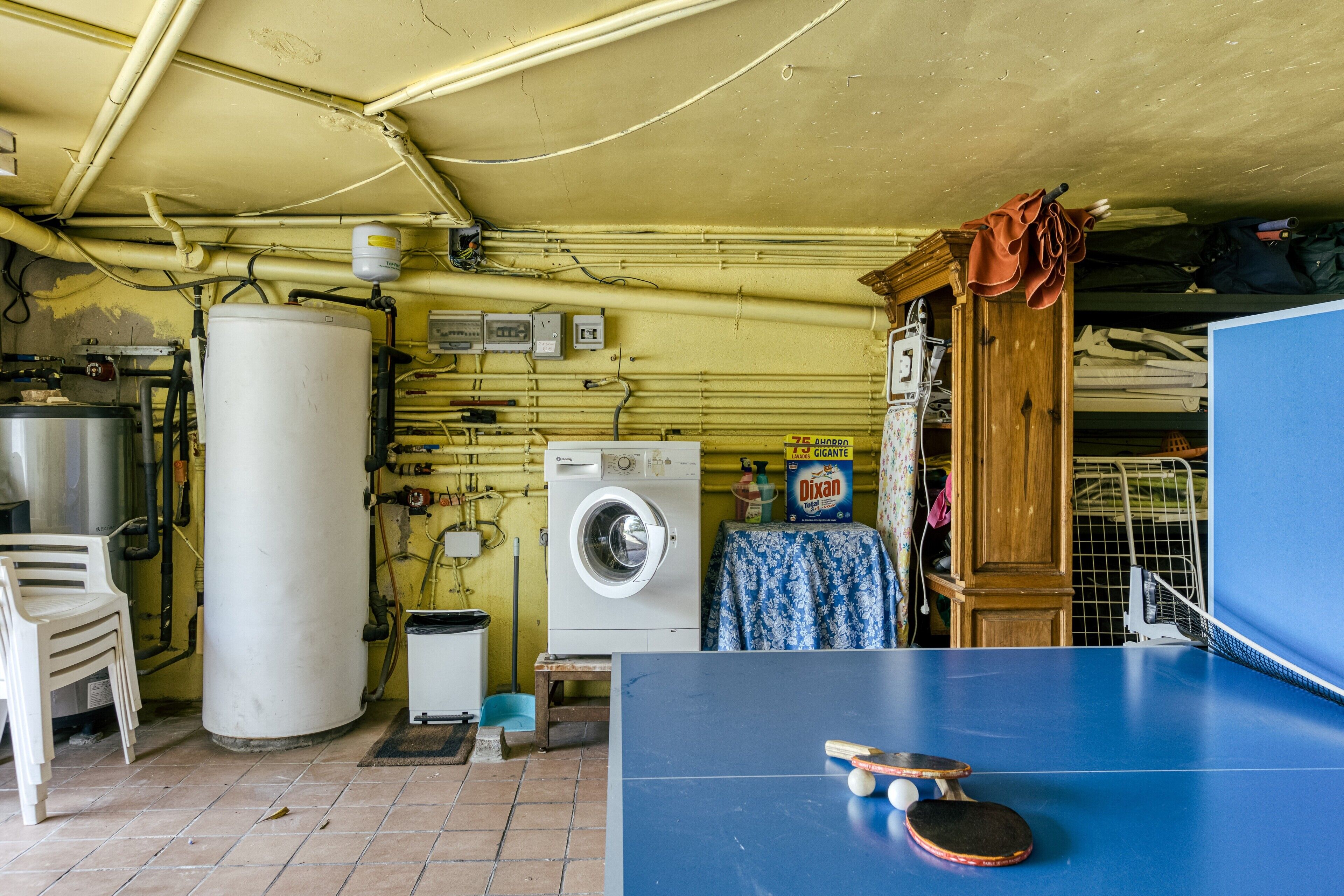 Een wasserette met een wasmachine, een groot boiler en een pingpongtafel.