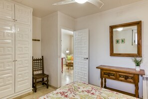 Un dormitorio con una cama, una silla de madera, un aparador y un espejo en la pared.
