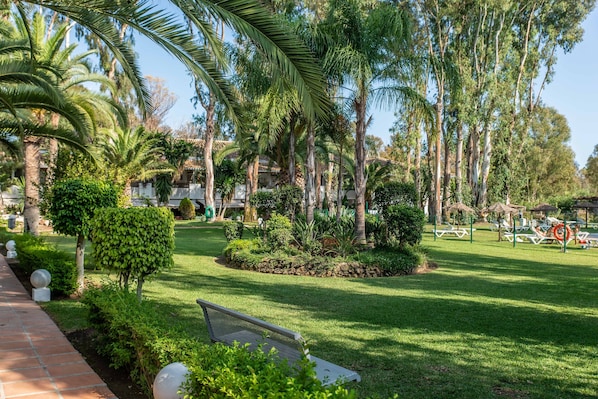 A well-maintained garden with a variety of trees, a paved walkway, and outdoor seating areas.