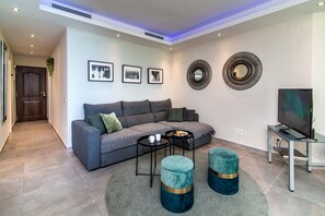 Un soggiorno moderno con un divano grigio, un tavolino da caffè, due poggiapiedi, una TV e decorazioni a parete.