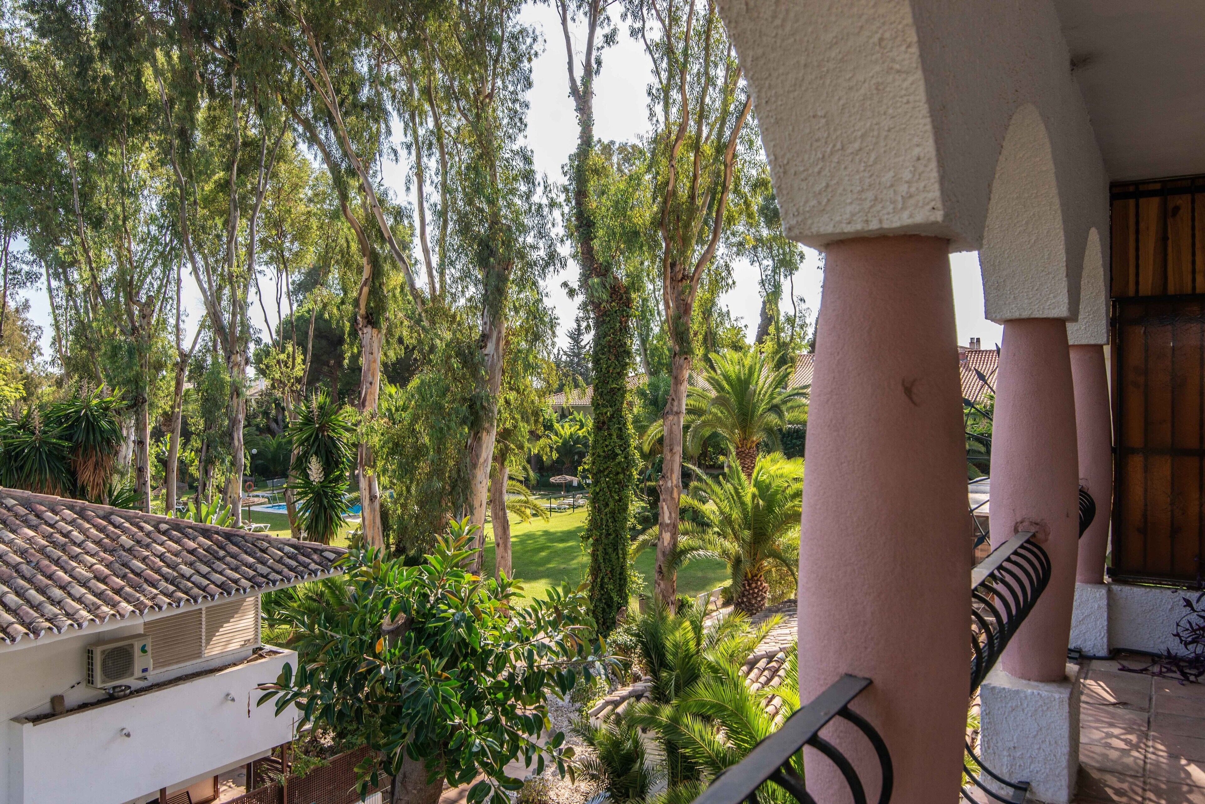 Un balcón con vista a un jardín, que incluye árboles y una piscina.